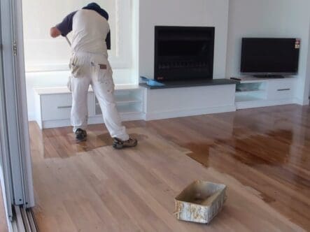 a man applying polyurethane coating on hardwood floor with mop.