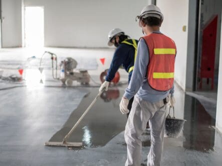 two professional workers applying floor finish on concrete floor in a commercial space with mop.