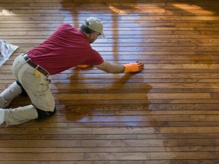 a man on his knees waxing a hardwood floor for shinning.